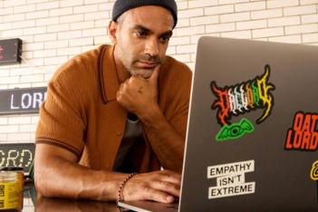 Man wearing a beanie and shirt works on a laptop.