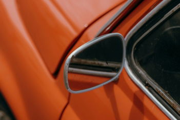 Side mirror reflecting a blurred background on an orange car